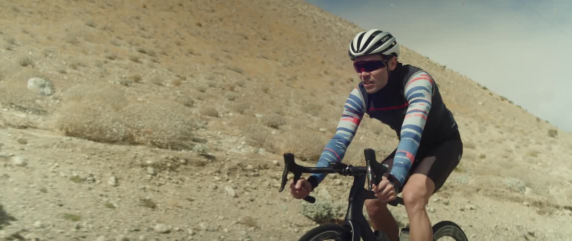 A man wearing a bicycle helmet and sunglasses is riding a bike near a mountain