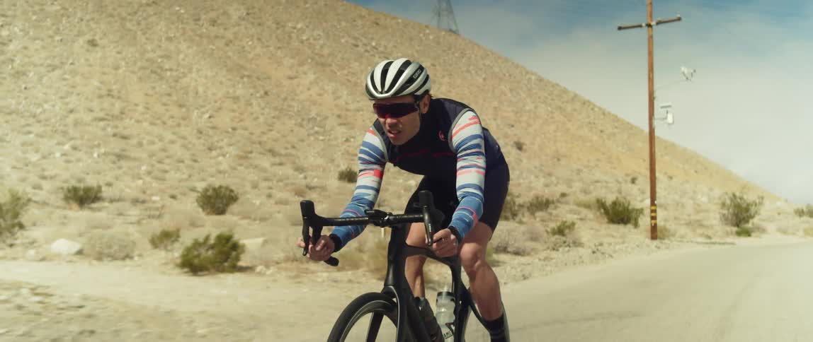 A man cycles along a road through badlands during the day