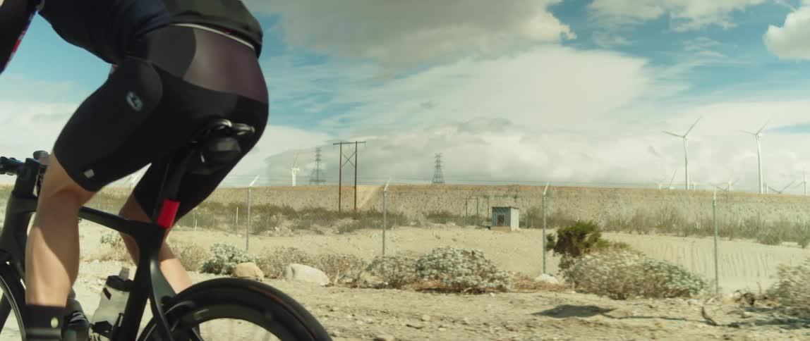 A cyclist rides a bicycle along a road through an arid countryside on a bright day