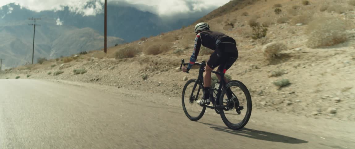 Man wearing a helmet rides a bicycle on a road in the desert close to the mountains