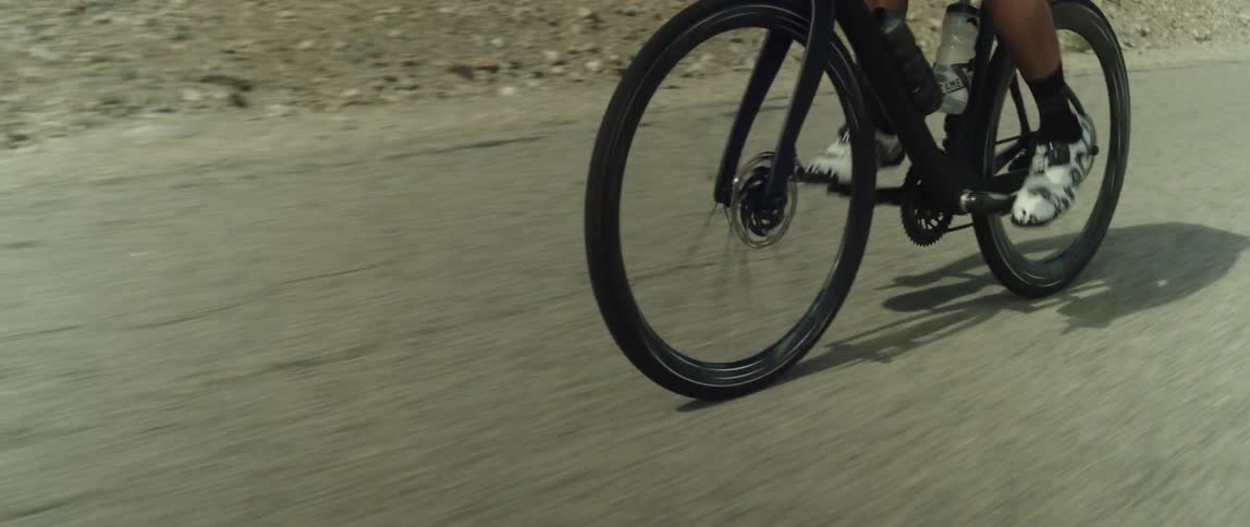 A cyclist pedals a bicycle along a road through an arid countryside during the day