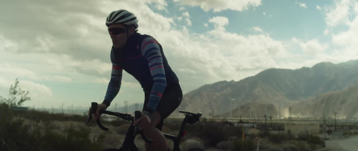 A cyclist pedals hard while cycling along a road through an arid countryside during the day