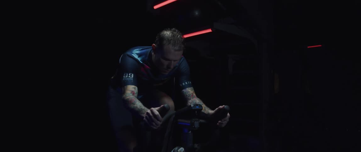 Male cyclist with jersey shirt and tattoos rides exercise bike