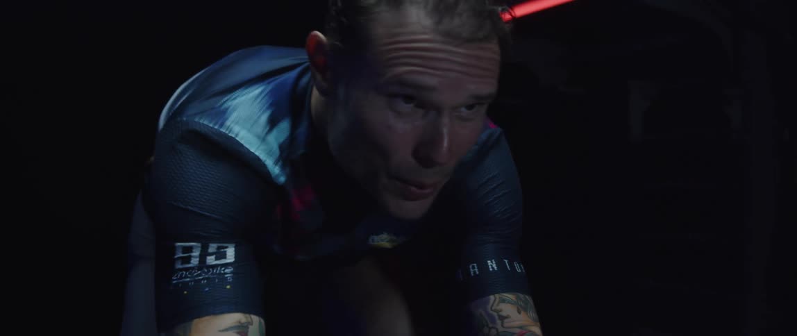 Determined and sweaty male cyclist with jersey shirt and tattoos rides exercise bike