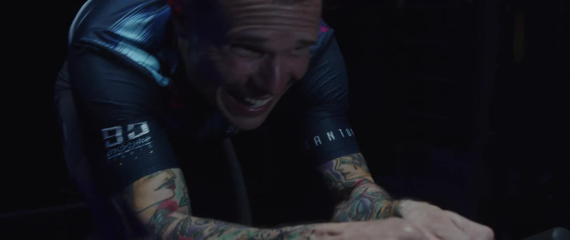 Determined male cyclist with jersey shirt and tattoos rides exercise bike