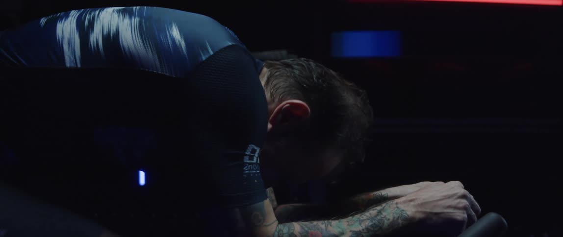 Man with tattooed sleeves sweats as he pedals on stationary bike
