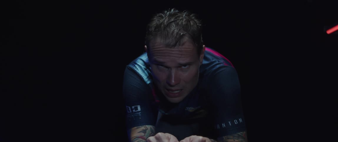 Man pedaling on a static bicycle inside a dimly lit room against a dark background