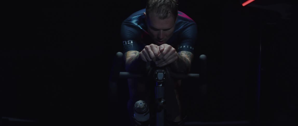 Man breathes deeply while pedaling stationary bicycle in dark room