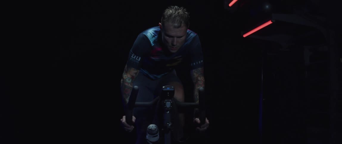 Focused sweaty man exercising on a stationary bike in a dark gym room