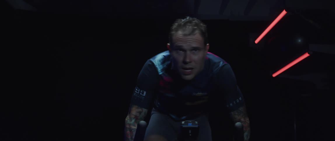 Man with tattoo sleeves pedals stationary bike in dark room