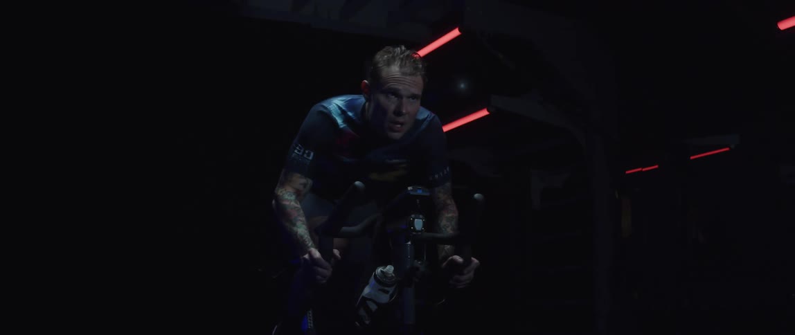 Man sweats while pedaling on stationary bike in dark room