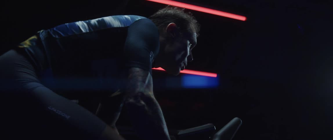 Man cycles indoor in dark room lit by neon lighting