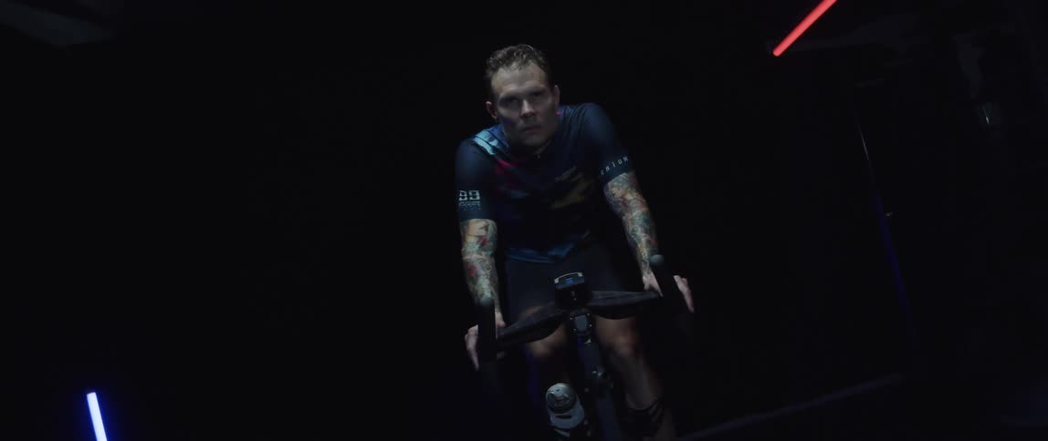 Focused man wearing a cycling jersey exercising on a stationary bike in a dark gym room