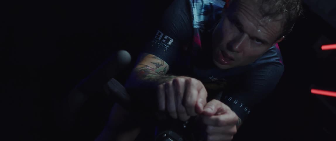 Determined and sweaty male cyclist with jersey shirt and tattoos rides exercise bike