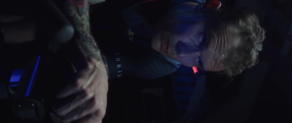 Focused sweaty man heavy breathing while exercising on a stationary bike in a dark gym room