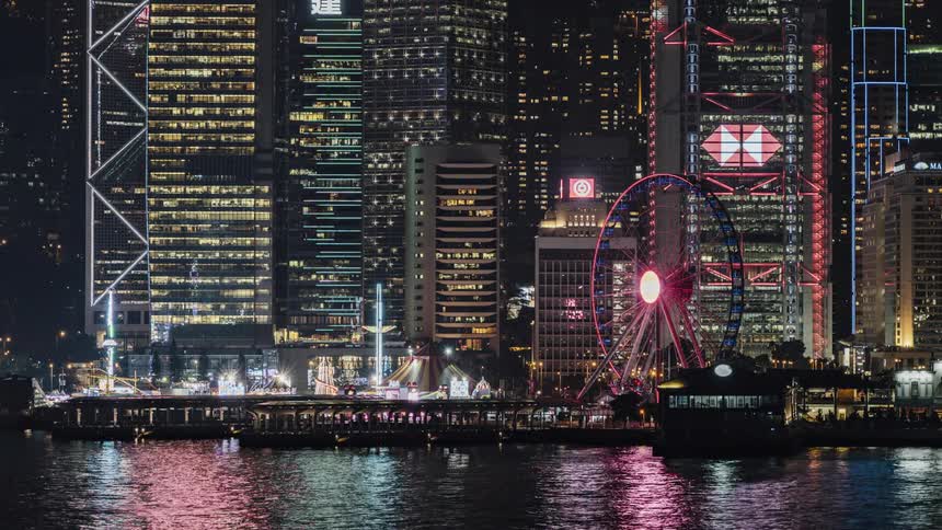 A light show on the hong kong skyscrapers at night with victoria harbor surface shimmering and reflecting color