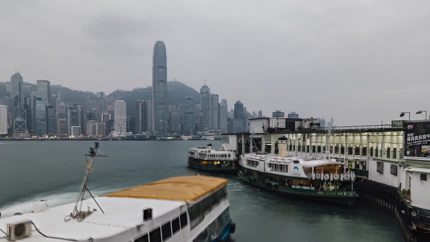 Daylight moves in as boats are sailing in the water and a big city with tall buildings and skyscrapers is in the distance