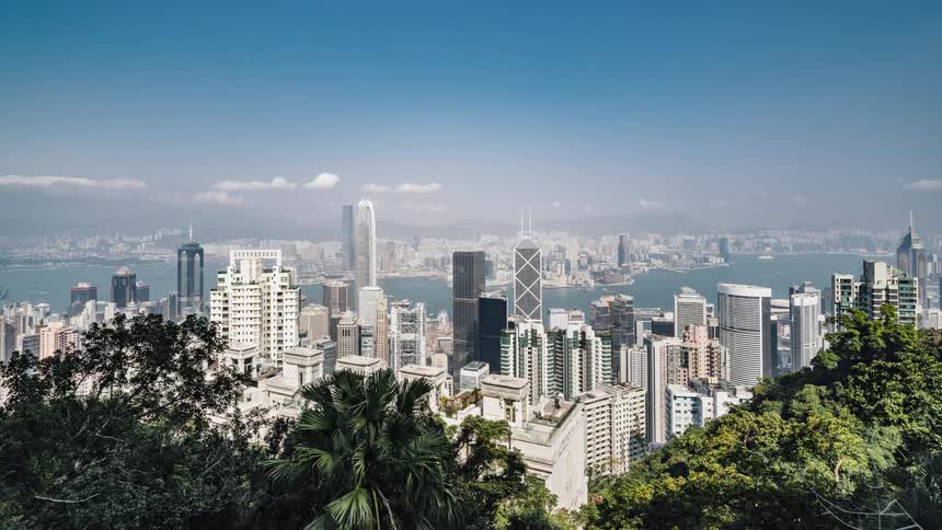 A boat sails past a dense city along the coast