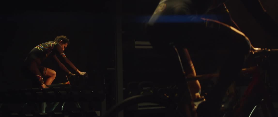 Man riding a static bicycle inside a dimly lit room reflected on a mirror