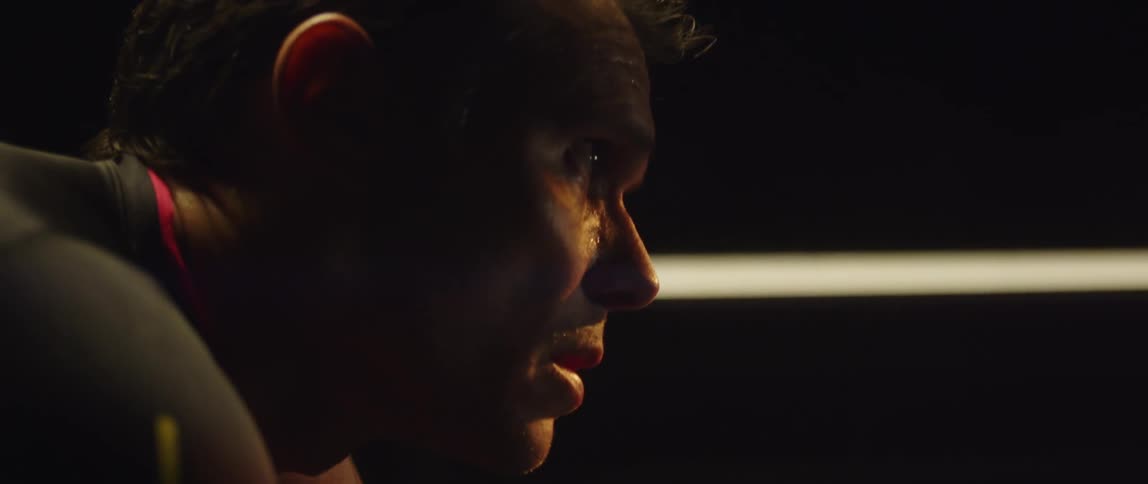 Close up of the face of a man pedaling a static bicycle inside a dimly lit room