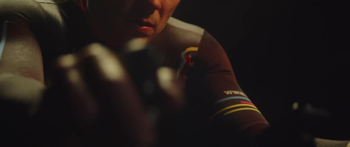 Man sweats while exercising on stationary bicycle in dark room