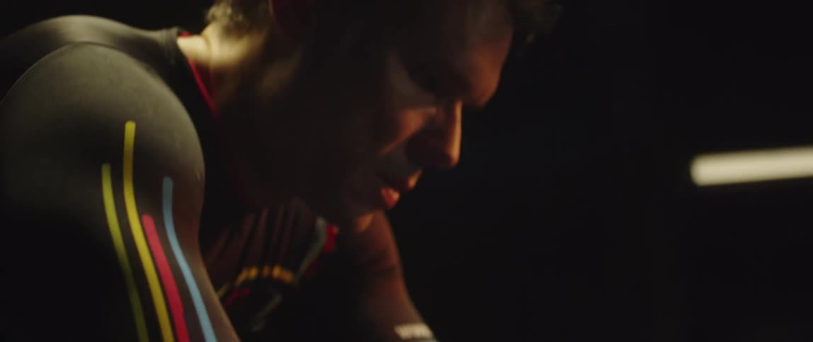 Athletic man wearing a long sleeve shirt riding a stationary bike in a dark room
