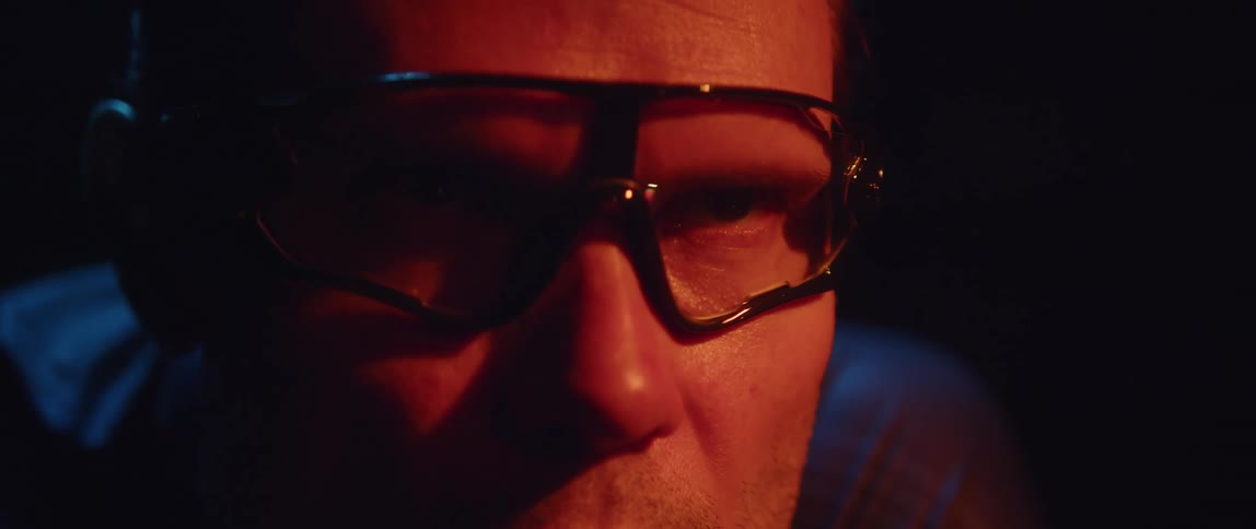 Determined man wearing cycling glasses with his face illuminated by a orange light opening his eye