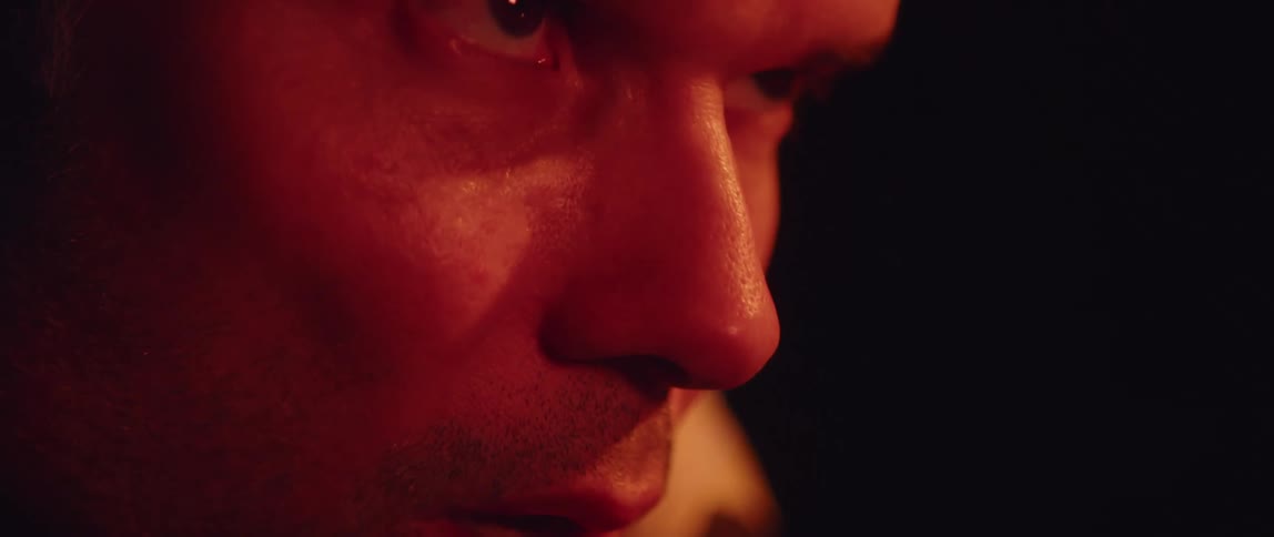 Sweaty man breathes deeply his face lit by red lighting in dark room