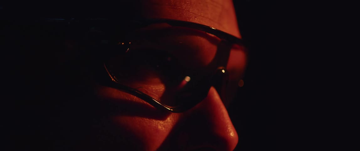 Close up of the profile of a man wearing sunglasses inside a dimly lit room