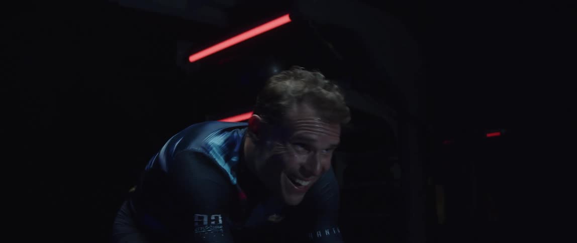 Tattooed man pedaling on a static bicycle inside a dimly lit room