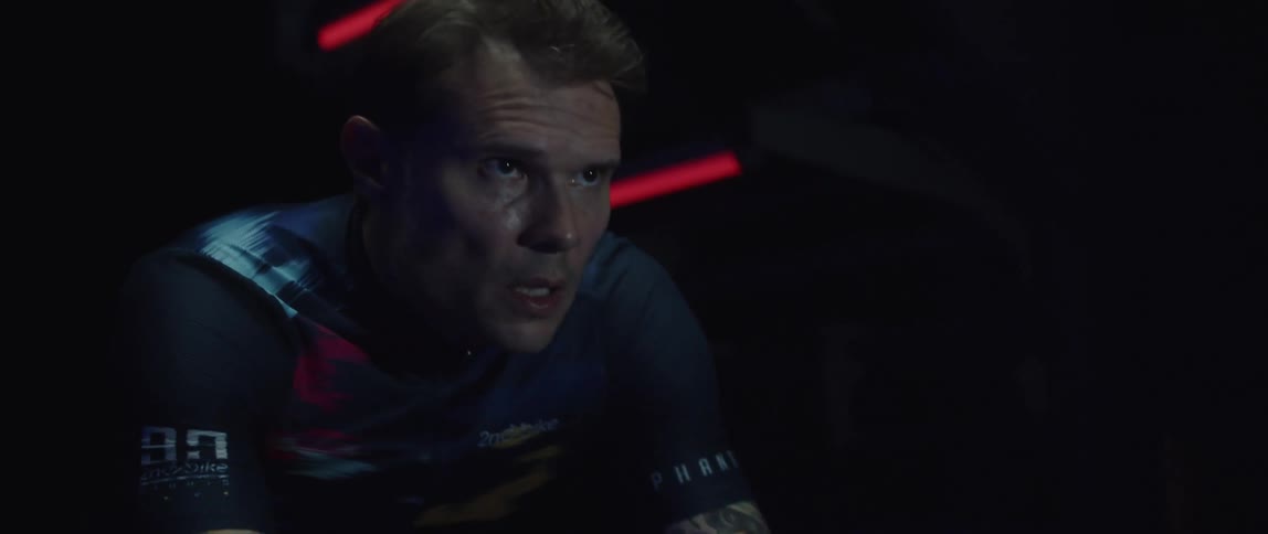 Determined male cyclist with jersey shirt and tattoos rides exercise bike