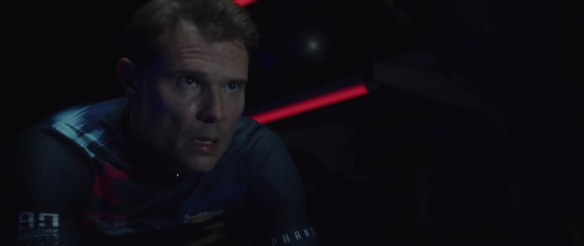 Man pedaling on a static bicycle inside a dimly lit room against a dark background