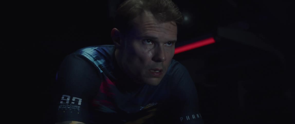 Focused sweaty man riding a stationary bike in a dark gym room