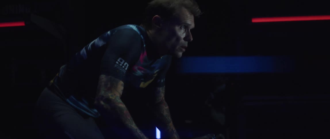 Man pedaling on a static bicycle inside a dimly lit room against a dark background