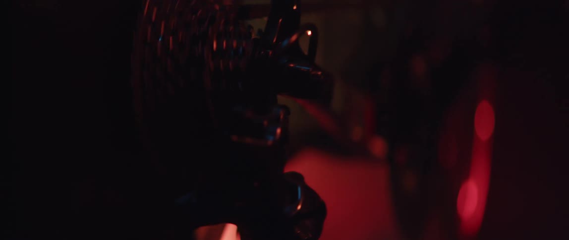 Close up of the gears and pedals of a static bicycle being pedaled inside a dimly lit room