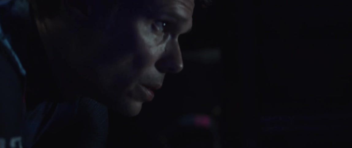 Focused cyclist man wearing a cycling jersey riding a stationary bike in a dark room