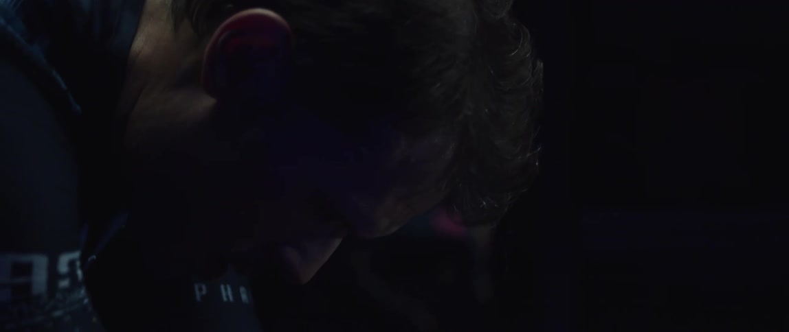 Focused sweaty athletic man exercising on a stationary bike in a dark gym room