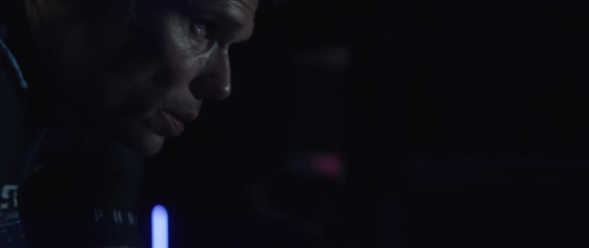 A tattooed man riding a stationary bike in darkness