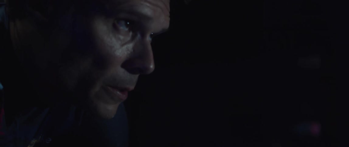 Tattooed man pedaling on a static bicycle inside a dimly lit room