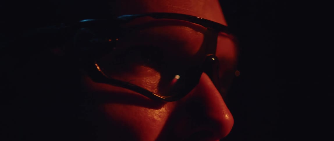Red spotlight is reflected in mans eyeglasses in a dark room