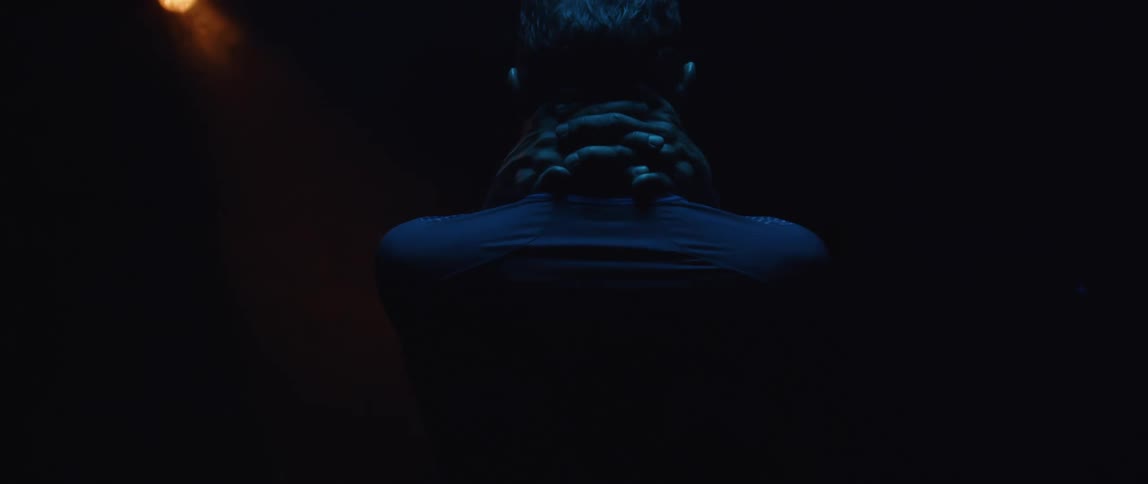 A young hispanic man is standing and has his hands around his neck