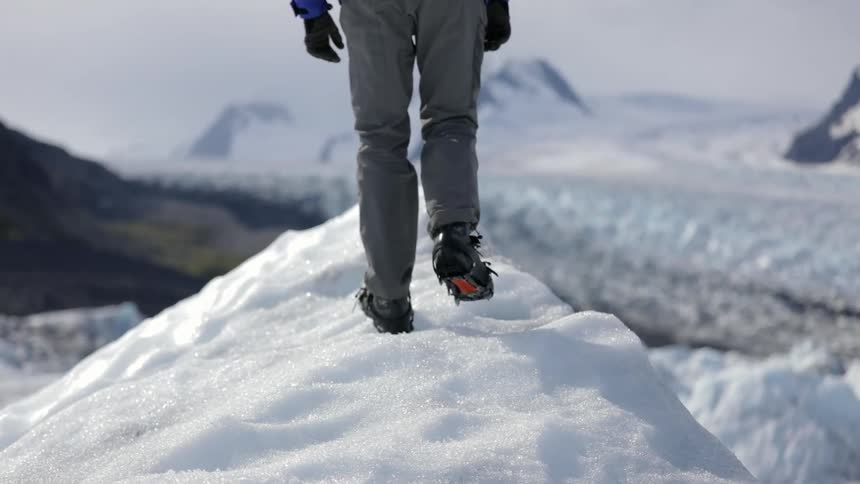 A man is climbs towards a cliff on some ice