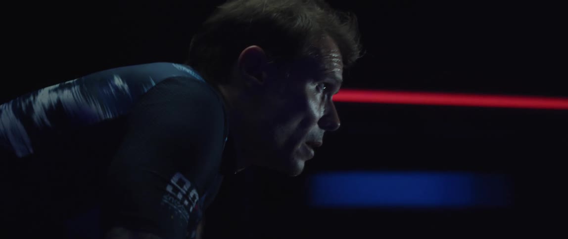 Focused sweaty man wearing a cycling jersey exercising on a stationary bike in a dark room