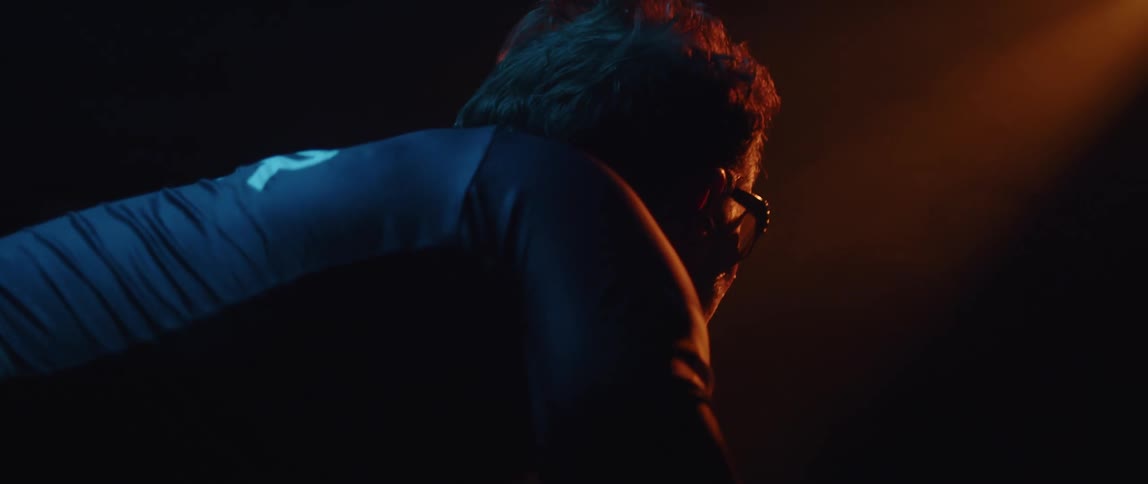 Colored lighting casts mans face into partial silhouette as he pedals in dark room
