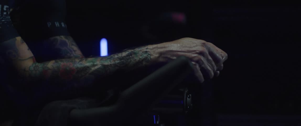 Mans hands and arms resting on the handlebar of the stationary bike he is exercising on