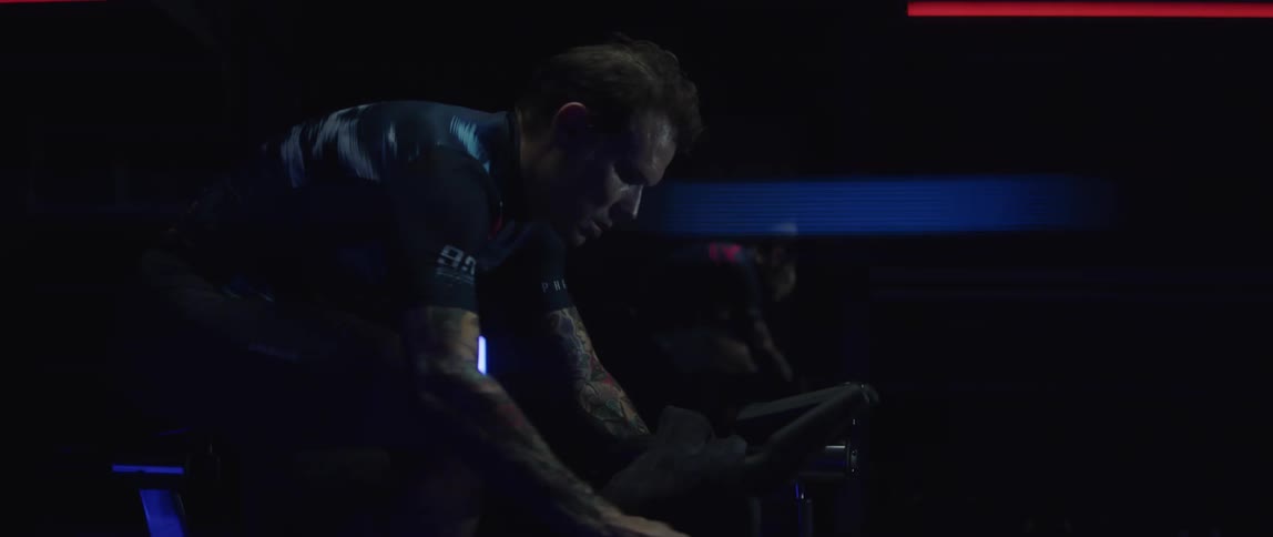 A tattooed man riding a stationary bike in front of a mirror