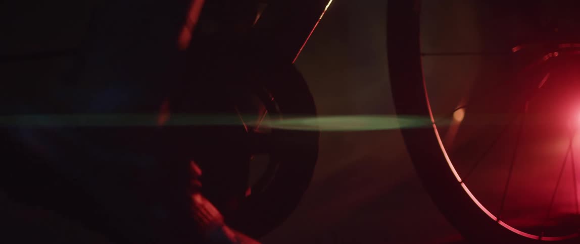 Close up of the gears and pedals of a static bicycle being pedaled inside a dimly lit room