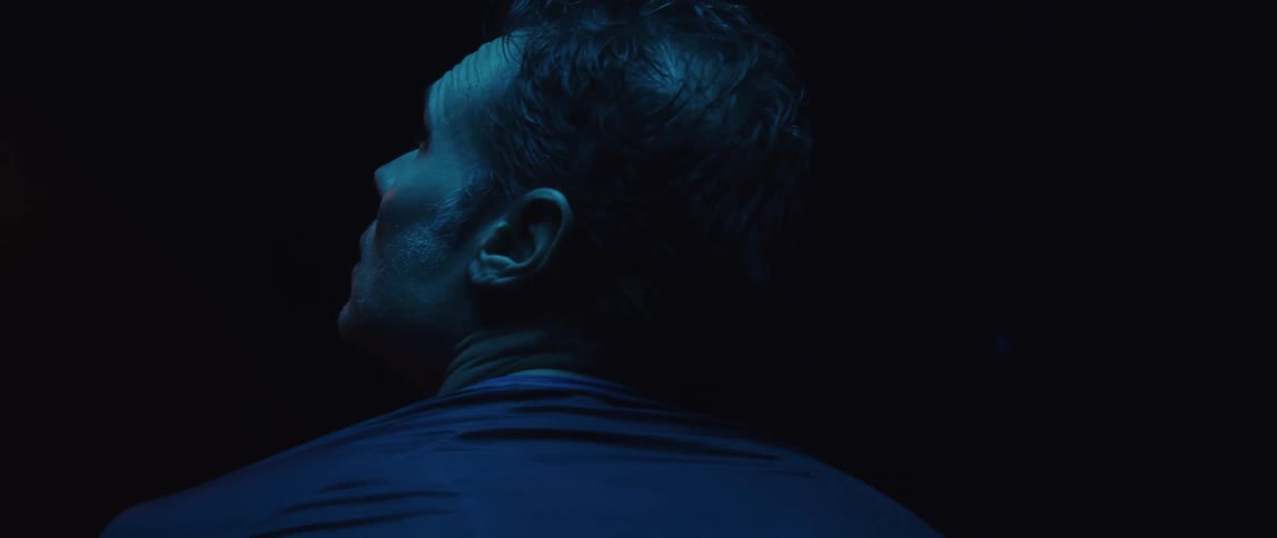 Man wearing shirt with two letters on the back looks up in dark room