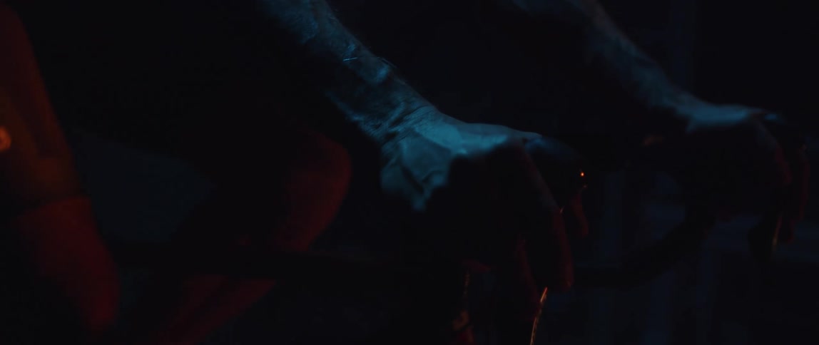 Knees of a man pedaling a static bicycle inside a dimly lit room