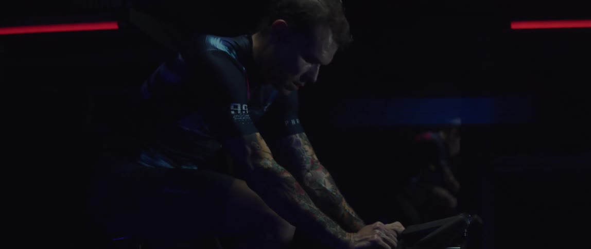 A tattooed man riding an indoor stationary bike